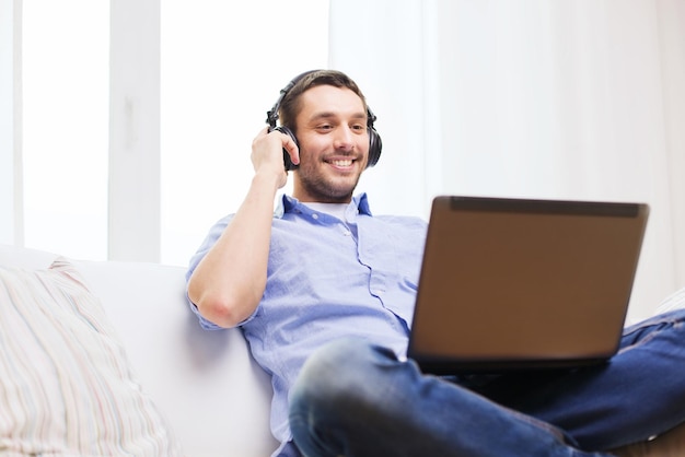 Conceito de tecnologia, casa, música e estilo de vida - homem sorridente com laptop e fones de ouvido em casa