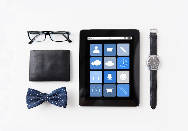 Foto conceito de tecnologia e objetos - computador tablet pc com ícones de aplicativos, carteira, óculos, gravata borboleta e relógio de pulso na mesa