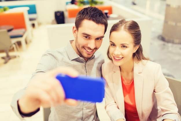 conceito de tecnologia e pessoas - casal feliz tomando selfie com smartphone no shopping ou café