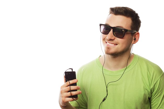 Conceito de tecnologia e pessoas jovem vestindo camiseta verde ouvindo música e usando smartphone isolado no branco