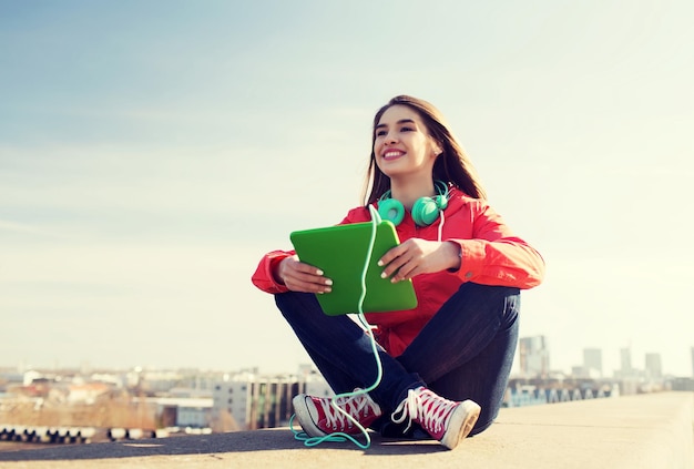 conceito de tecnologia, estilo de vida, música e pessoas - jovem sorridente ou adolescente com computador tablet pc e fones de ouvido ao ar livre