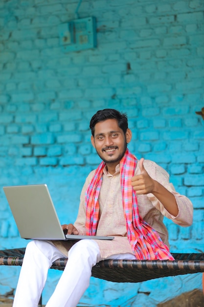 Conceito de tecnologia: fazendeiro indiano usando laptop e aparecendo em casa