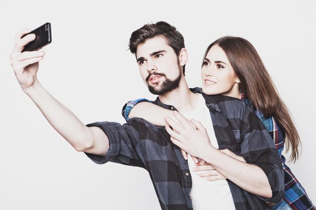 Conceito de tecnologia, internet, emocional e pessoas: jovem casal amoroso feliz fazendo selfie e sorrindo em pé contra um fundo branco. tonalidade na moda especial.