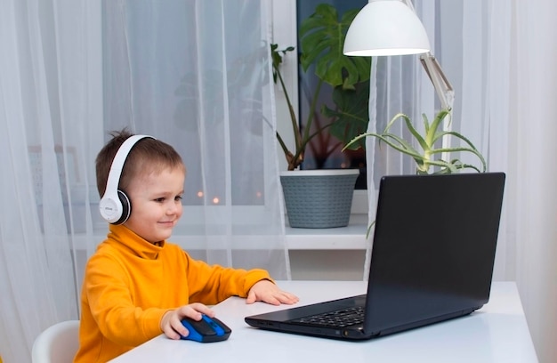 Conceito de tecnologia, jogos e pessoas - um menino com fones de ouvido jogando videogame em um computador em casa à noite. o conceito de desenvolvimento infantil, infância, comunicação online.