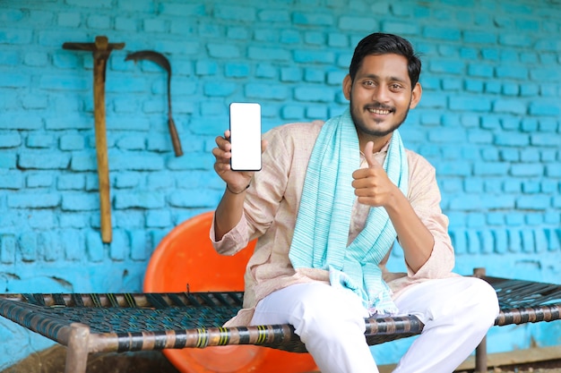 Conceito de tecnologia: jovem fazendeiro indiano mostrando smartphone em casa