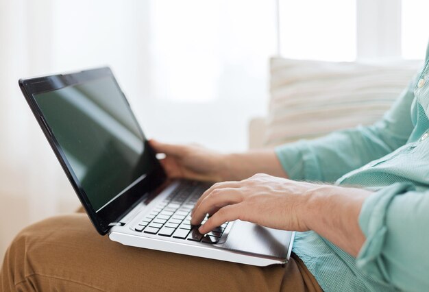 conceito de tecnologia, lazer, propaganda e estilo de vida - close-up do homem trabalhando com computador portátil e sentado no sofá em casa