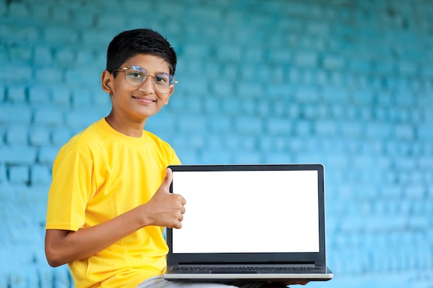 Conceito de tecnologia: menino de escola indiano fofo usando laptop e mostrando golpes