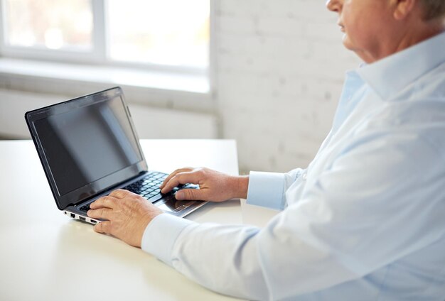 Conceito de tecnologia, negócios, aposentadoria, pessoas e lazer - close-up de homem sênior com computador portátil digitando na mesa no escritório