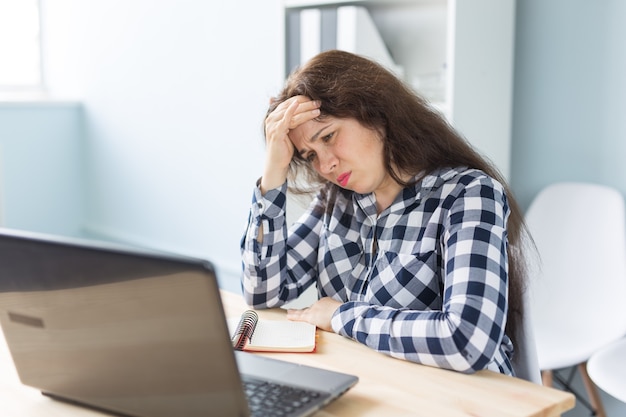 Conceito de tecnologia, negócios e pessoas - jovem mulher perplexa com a mão perto da testa, sentada em frente ao laptop