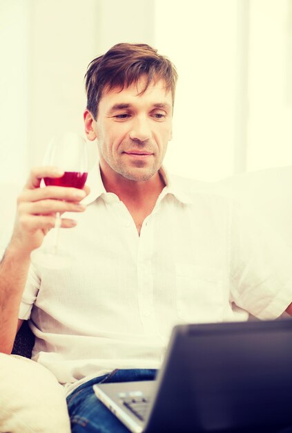 conceito de tecnologia, negócios, lazer, bebidas, aposentadoria e estilo de vida - homem feliz com um laptop e uma taça de vinho rosé em casa