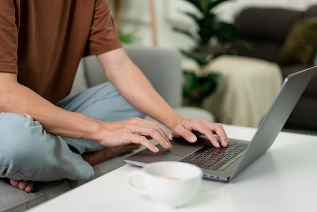 Conceito de tecnologia O homem de camiseta marrom concentrando-se em digitar algo em seu computador portátil