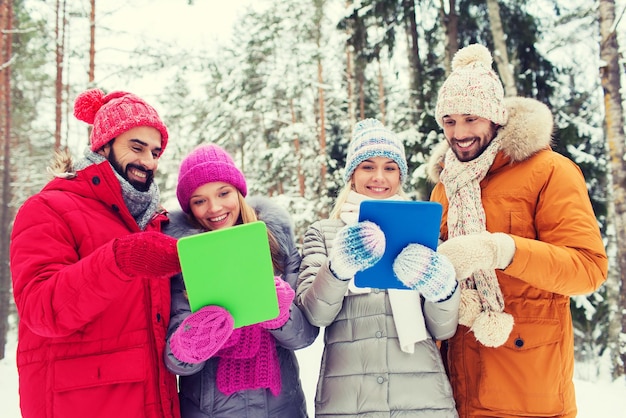 Foto conceito de tecnologia, temporada, amizade e pessoas - grupo de homens e mulheres sorridentes com computadores tablet pc na floresta de inverno