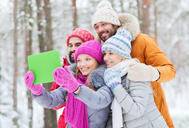 conceito de tecnologia, temporada, amizade e pessoas - grupo de homens e mulheres sorridentes tomando selfie tablet pc computador na floresta de inverno