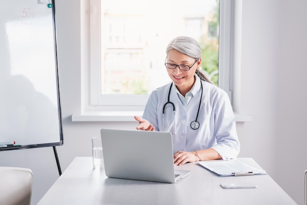 Conceito de telemedicina Médica sênior falando com paciente usando webinar de vídeo online de laptop