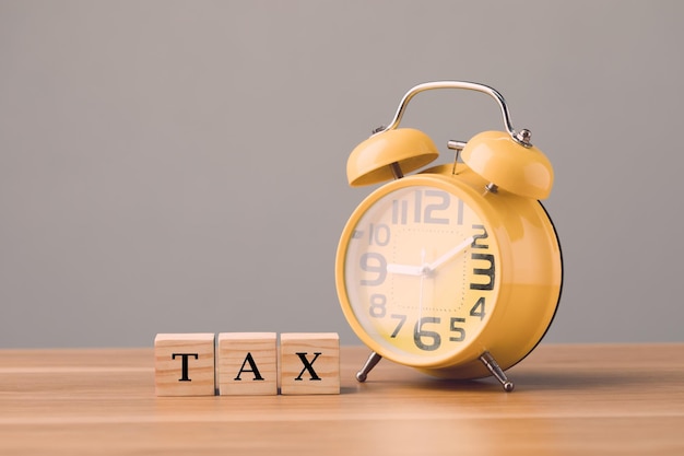 Foto conceito de tempo de pagamento de impostos imposto escrito em blocos de madeira dispostos na mesa de escritório e relógio amarelo com parede cinza idéias financeiras de negócios