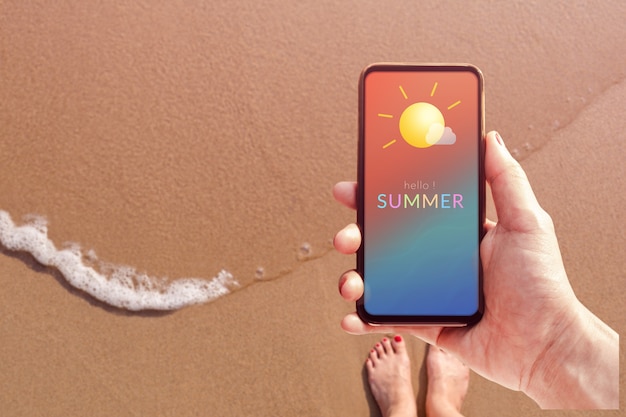 Conceito de temporada de verão. Mulher segurando o telefone móvel com a mensagem de verão e o ícone do tempo. Praia de areia com luz solar como pano de fundo. Vista do topo