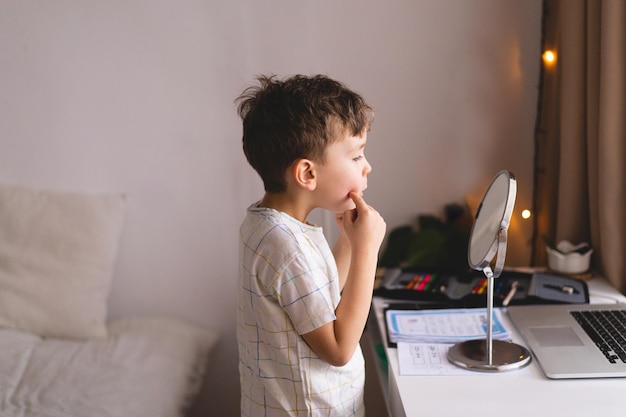 Conceito de terapia da fala Menino bonitinho pronunciando o som O olhando para o espelho fazendo uma aula de terapia da fala online através de um laptop