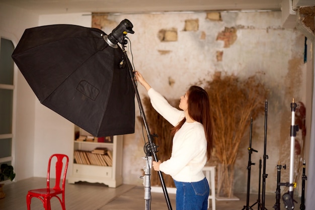 Conceito de trabalho criativo em estúdio fotográfico mulher configurando equipamento fotográfico