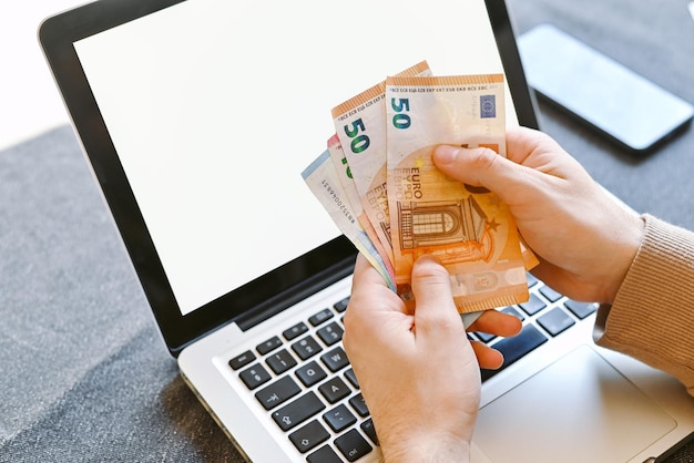 Conceito de trabalho freelance close-up de mãos segurando novas notas de euro ganhas trabalhando no laptop em casa