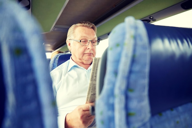 Foto conceito de transporte, turismo, viagem e pessoas - homem sênior lendo jornal em ônibus de viagem