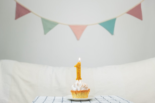 Conceito de um ano de idade. Vela de aniversário "One" acesa no topo de um pequeno bolo em um fundo elegante decorado