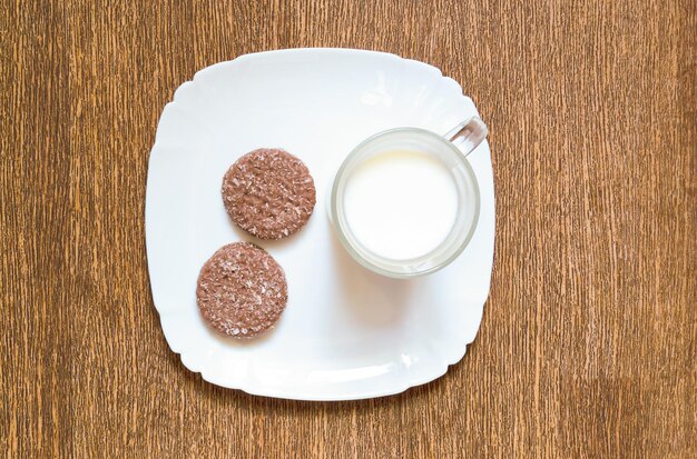 Conceito de um pequeno-almoço ligeiro. Cookies de chocolate com um copo de leite em um prato