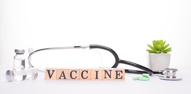 Conceito de vacinação. Feche a foto da vista panorâmica do banner de recipientes de vidro de pílulas de ferramentas médicas com vacina e blocos de madeira fazendo vacina de palavra em pano de fundo branco