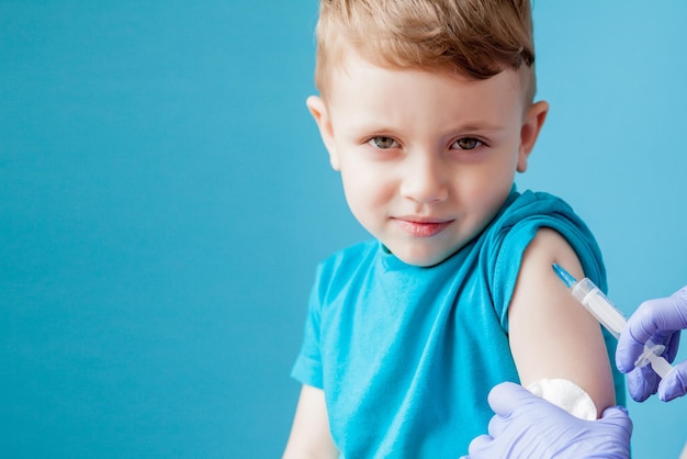 Foto conceito de vacinação médica vacinando menino bonitinho sobre fundo azul fechado
