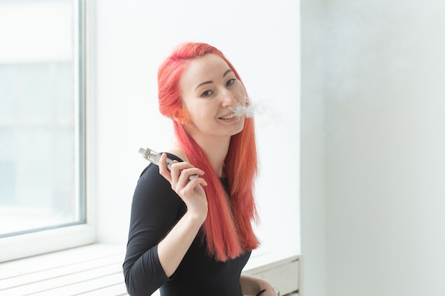 Conceito de vape, vício e pessoas - mulher de cabelo vermelho está fumando vape.