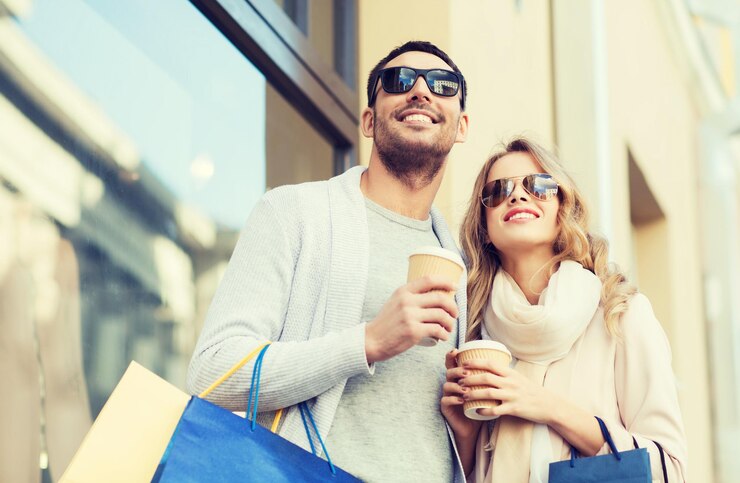 Foto conceito de venda, consumismo e pessoas - casal feliz com sacolas de compras e copos de papel de café na vitrine na rua da cidade