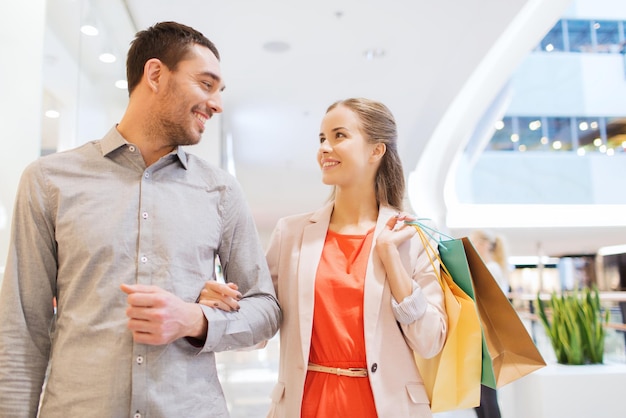 Conceito de venda, consumismo e pessoas - casal jovem feliz com sacolas de compras andando e conversando no shopping