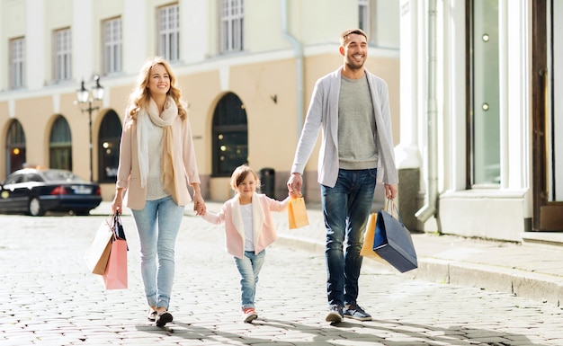 conceito de venda, consumismo e pessoas - família feliz com criança e sacolas de compras na cidade