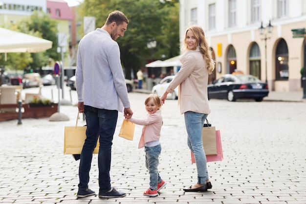 conceito de venda, consumismo e pessoas - família feliz com criança e sacolas de compras na cidade