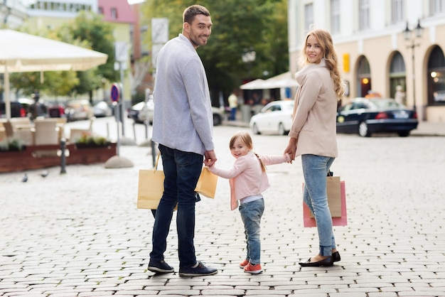 conceito de venda, consumismo e pessoas - família feliz com criança e sacolas de compras na cidade