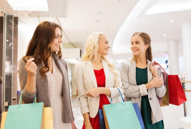 conceito de venda, consumismo e pessoas - mulheres jovens felizes com sacolas de compras falando no shopping