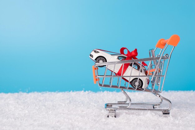 Conceito de venda de inverno. Feche a foto do mini carro branco de brinquedo em um carrinho de compras em miniatura na neve isolado em um fundo azul