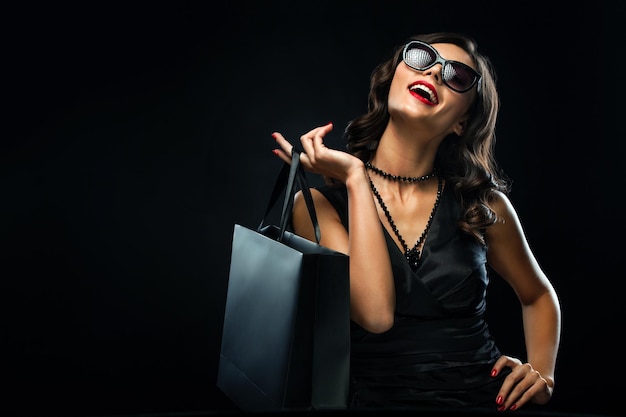 Conceito de venda de sexta-feira negra Mulher de compras segurando saco cinza isolada em fundo escuro em feriado