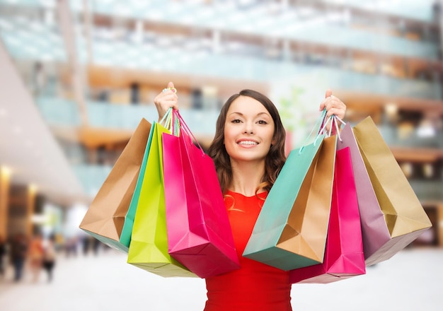 conceito de venda, presentes, feriados e pessoas - mulher sorridente com sacos coloridos sobre fundo de centro comercial