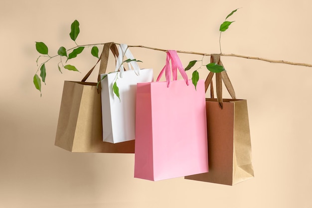 Foto conceito de vendas e descontos de verão ou primavera em um fundo bege sacolas de papel penduradas em um galho