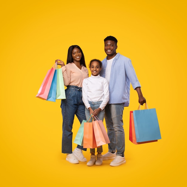 Conceito de vendas sazonais Família afro-americana feliz de três posando com sacolas de compras sobre fundo amarelo