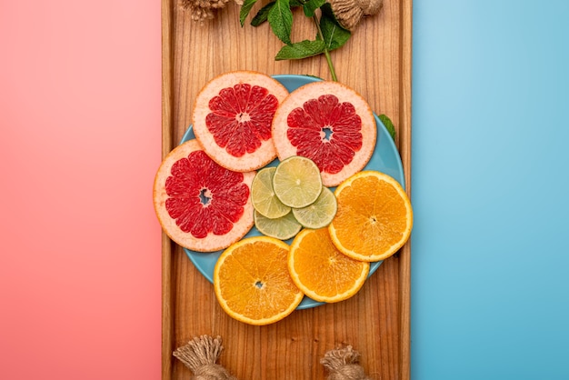 Conceito de verão fatiado toranja, laranja e limão na bandeja de madeira em fundo rosa e azul