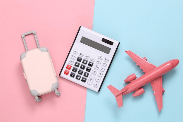 Conceito de viagem Calculadora avião e bagagem em um fundo bluepink Vista superior Flat lay