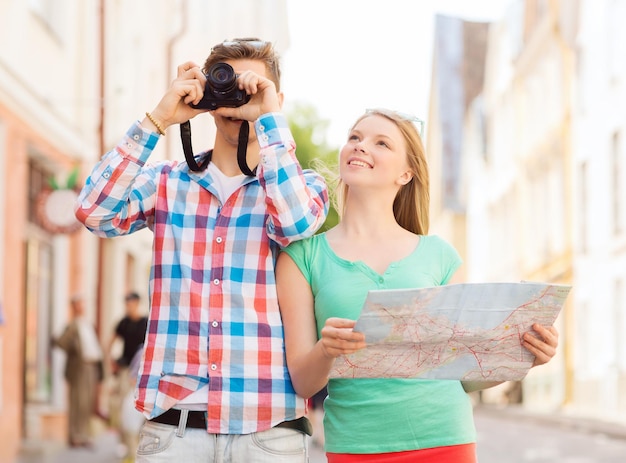 Foto conceito de viagem, férias, tecnologia e amizade - casal sorridente com mapa e câmera fotográfica explorando a cidade