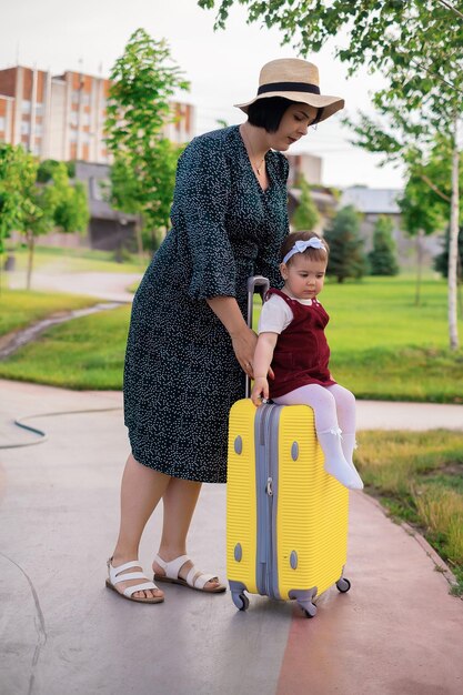 Foto conceito de viagem mãe e filha com uma mala estão se preparando para uma viagem em que uma criança se senta em uma mala