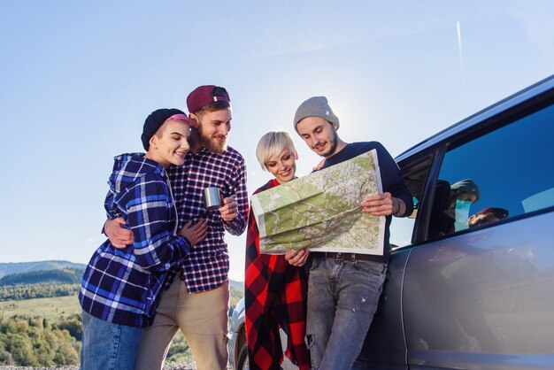 Conceito de viagens de verão. Amigos felizes usando o mapa de papel perto de carro alugado na natureza.