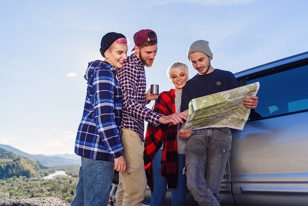 Conceito de viagens de verão. amigos felizes usando o mapa perto de carro alugado na natureza.