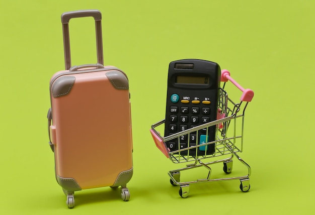 Conceito de viagens e compras. Mini mala de viagem de plástico e carrinho de supermercado com calculadora sobre fundo verde.