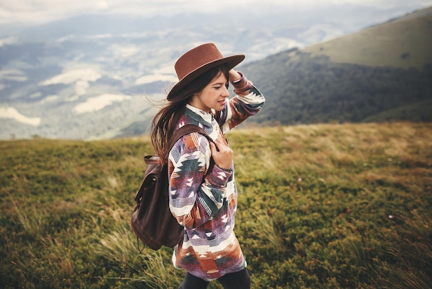 Conceito de viagens e desejo de viajar Menina elegante hipster de chapéu andando no topo das montanhas Jovem feliz com mochila explorando montanhas enevoadas Incrível momento atmosférico
