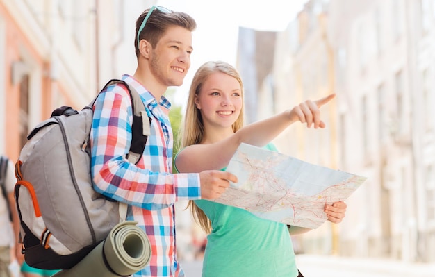 conceito de viagens, férias e amizade - casal sorridente com mapa e mochila na cidade