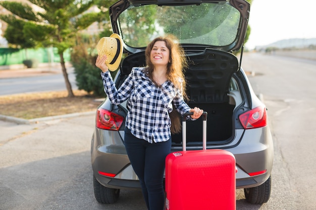 Conceito de viagens, férias e pessoas. jovem em pé perto de carro com chapéu com mala vermelha. Ela está pronta para viajar.